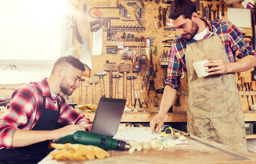 carpenters with laptop and blueprint at workshop - Credit to https://www.thehousewire.com/