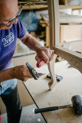 An old man carving wooden furniture in a workshop