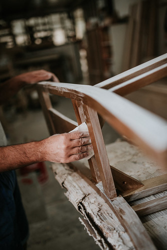 Carpenter sanding a chair with sandpaper in a small workshop