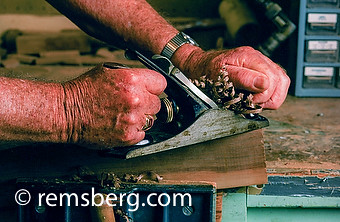 Close up older man planing wood.