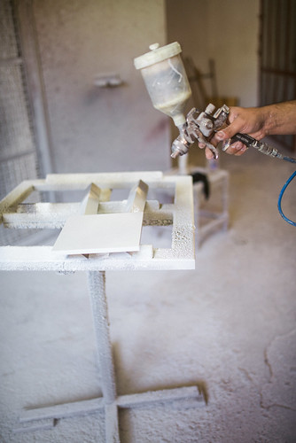 Applying white paint to a small piece of wood with a spray gun