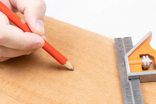 Hand with pencil and combination square on the wooden board